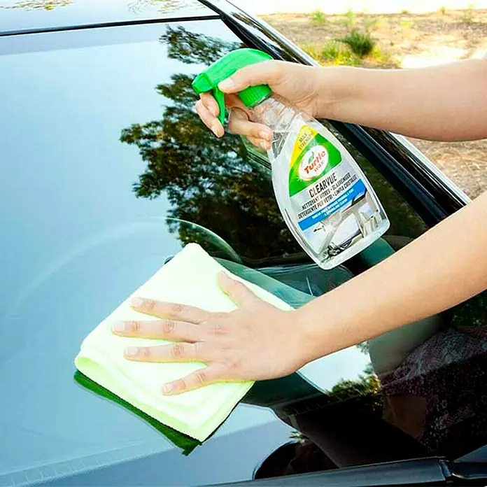 Turtle Wax Limpiacristales para coches Clearvue - 500 ml - Una persona limpiando el parabrisas de un coche con limpiacristales Turtle Wax ClearVue y un paño de microfibra.