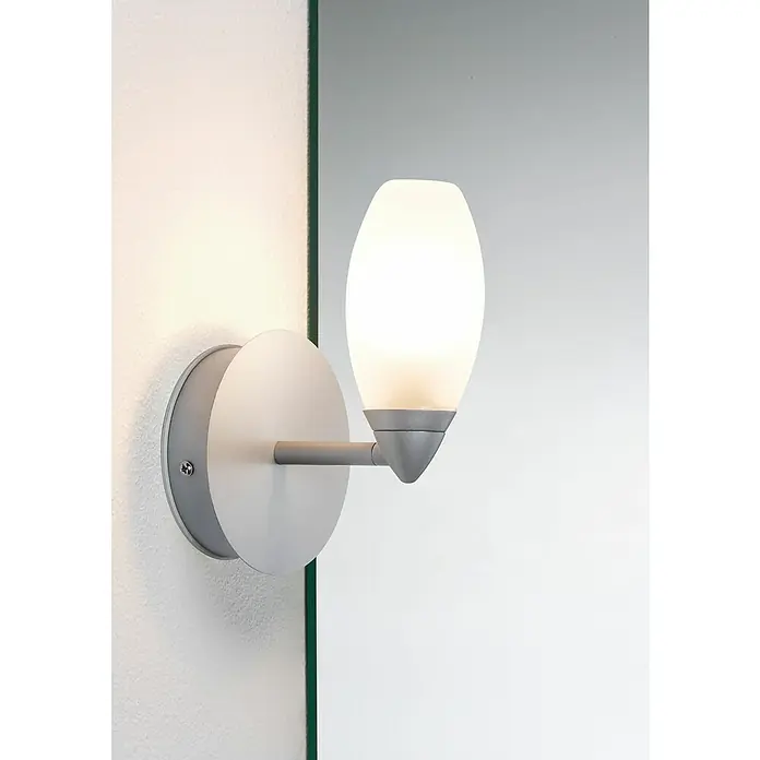 Paulmann Wandleuchte Carina - 28 W, L x B x H: 11,5 x 10,5 x 15,7 cm, Chrom, G9 - Diese Nahaufnahme zeigt eine moderne, silberne Wandleuchte mit einem leuchtenden, ovalen Lampenschirm an einer weißen Wand.