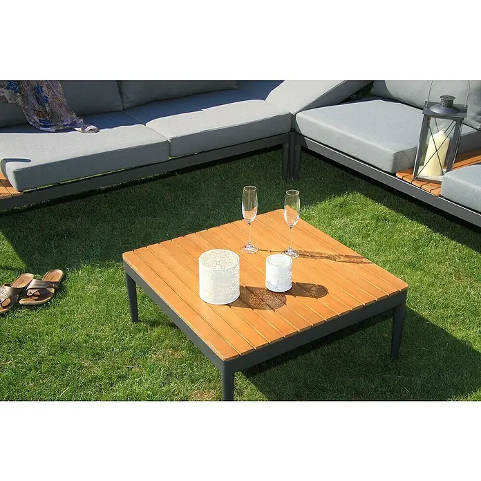 Acamp Loungemöbel-Set Paros - 4 -tlg., Akazie, Anthrazit, Braun, Silbergrau - Quadratischer Couchtisch aus Holz mit dekorativen Laternen und Champagnergläsern auf einem Rasen.
