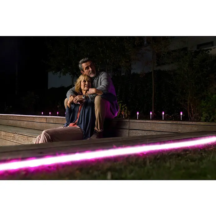 Ledvance Smart+ WiFi Smart-LED-Band Neon - Länge: 5 m, RGBW, 20 W, 630 lm - Ein Paar sitzt auf einer Treppe mit strahlenden, pinkfarbenen LED-Gartenleuchten für stimmungsvolle Beleuchtung im Freien.
