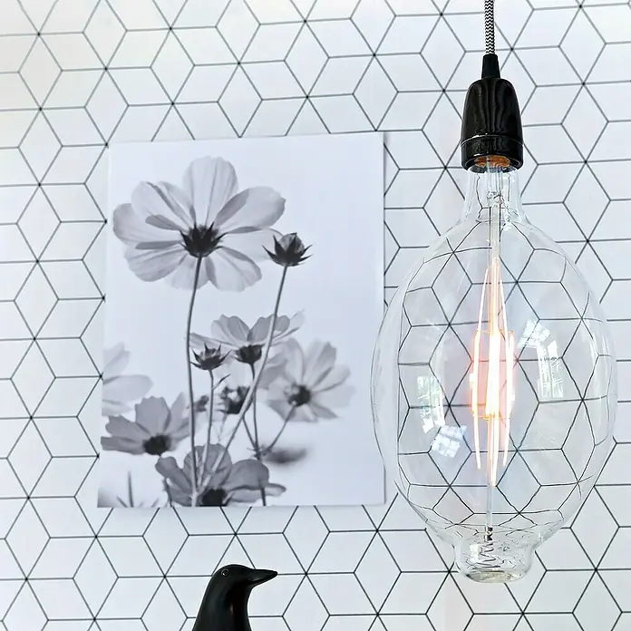 Home Sweet Home Lampenfassung Posh - E27, Schwarz, Keramik, Ø x H: 4,8 x 5,8 cm - Nahaufnahme einer dekorativen Glühbirne mit einem geometrischen Drahtkäfig um das Leuchtmittel, hängt vor einer Wand mit Würfelmuster.