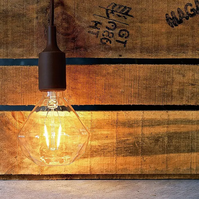 Home Sweet Home Lampenhülse - Braun, Gummi - Die edle Dekolampe mit ihrem warmen Licht erhellt jeden Raum. Die moderne Glühbirne ist ein echter Hingucker vor der rustikalen Holzwand.