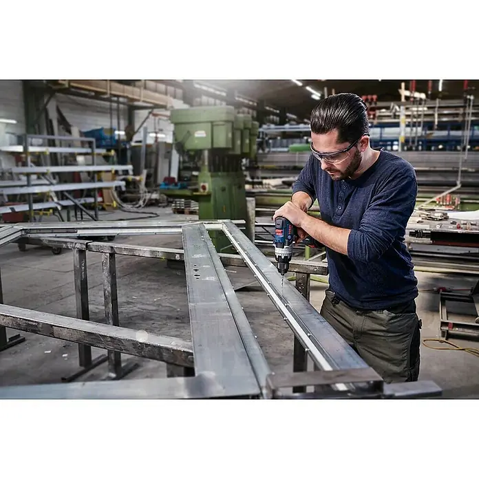 Bosch Broca para metal PointTeQ - 10 ud., Diámetro de la broca: 1,4 mm - Un hombre perfora agujeros en una pieza de metal en un taller usando un taladro Bosch azul. Lleva gafas de seguridad para protegerse.