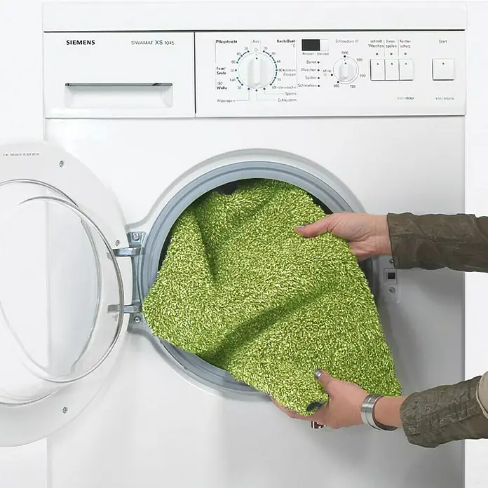 Astra Schmutzfangmatte entra SAUGSTARK - Grün, 75 x 130 cm, Material Nutzschicht: 100 % Baumwolle - Eine grüne Matte wird in eine weiße Siemens Waschmaschine gelegt.