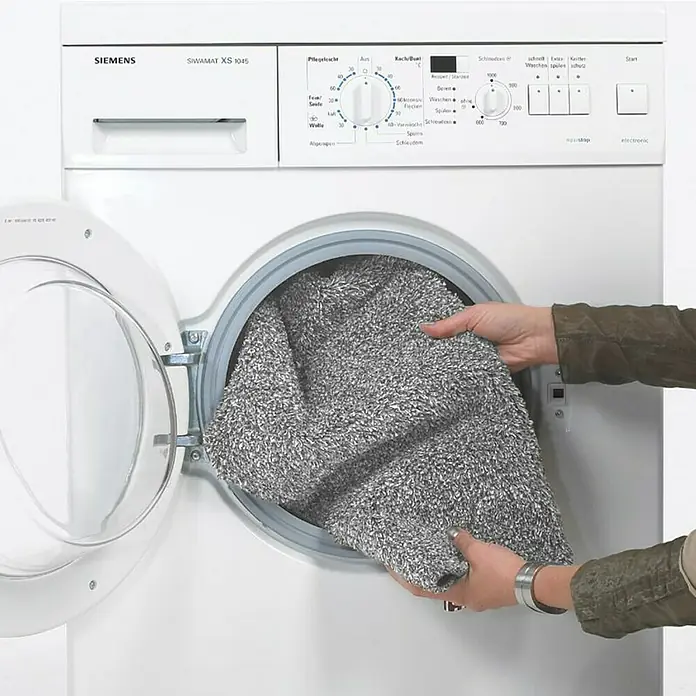Astra Schmutzfangmatte entra SAUGSTARK - Dunkelgrau, 75 x 130 cm, Material Nutzschicht: 100 % Baumwolle - Siemens Waschmaschine mit geöffneter Tür, in die eine Person einen grauen Teppich legt.\n