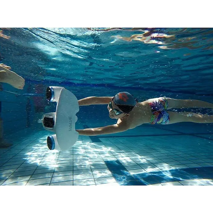 Sublue Tauchscooter White Shark - L x B x H: 465 x 230 x 230 mm - Unterwasseransicht eines Kindes, das im Pool mit einem Sublue Wasserscooter schwimmt. Der Scooter ist weiß und hat zwei Propeller.