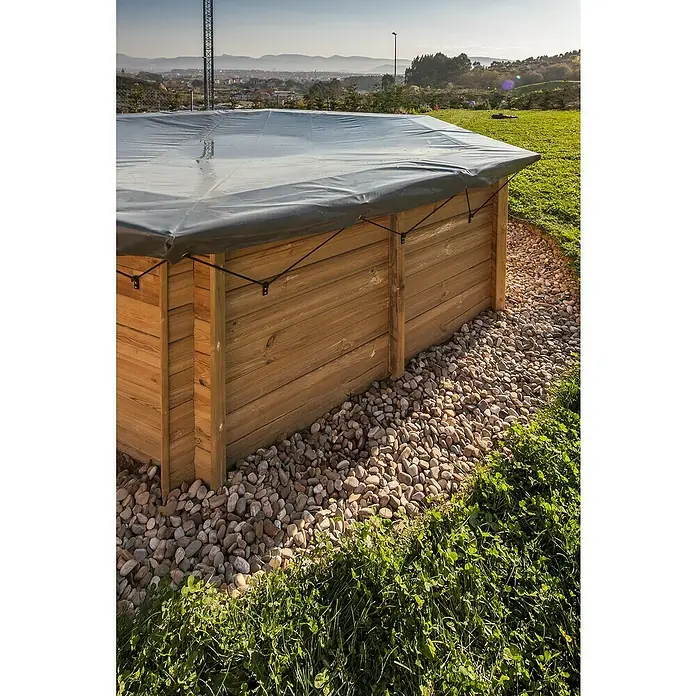 Gre Pool-Abdeckplane WinterL x B: 677 x 452 cm, Kunststoff - Das Bild zeigt eine Holzkiste mit einer wasserdichten Abdeckung, umgeben von Steinen und Gras in einer malerischen Landschaft.