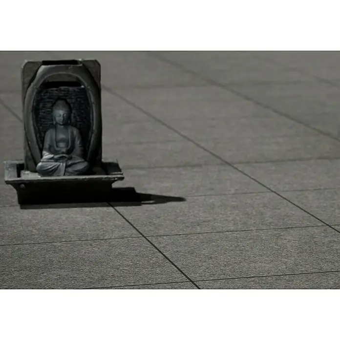 Feinsteinzeugfliese Recon - 60 x 60 cm, Schwarz, Matt - Nahaufnahme einer kleinen Buddha-Statue in einem dunklen Schrein, der auf einer gefliesten Oberfläche steht und einen friedlichen Akzent setzt.