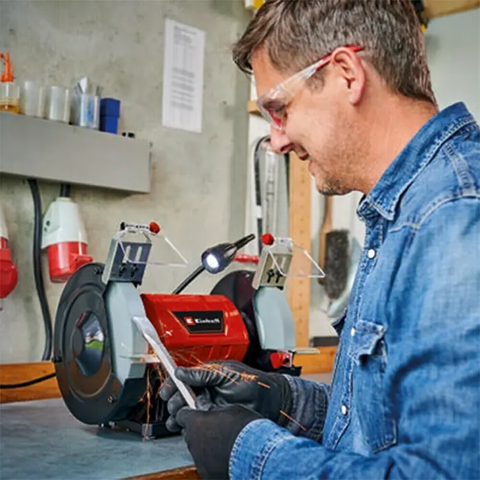 Einhell Esmeriladora doble eléctrica TC-BG 200 L - 400 W, 2.980 r.p.m. - Primer plano de un hombre usando una esmeriladora de banco Einhell, con gafas de seguridad y guantes puestos.