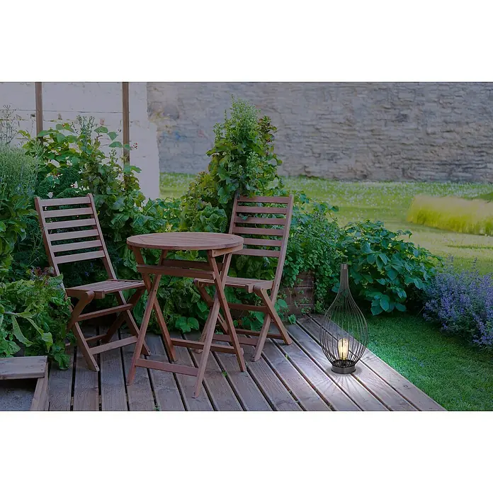 Globo Solar-Dekoleuchte - 0,06 W, Schwarz, Amber, IP44 - Eine elegante, schwarze Laterne beleuchtet eine Terrasse mit Holzboden, umgeben von Pflanzen und einem Tisch mit zwei Stühlen.