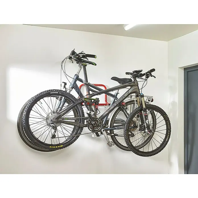 Mottez Fahrrad-Wandhalter - Geeignet für: 2 Fahrräder, Rot, Klappbar - Zwei Fahrräder hängen an einer Fahrradaufhängung an einer weißen Wand. Die Fahrräder sind Mountainbikes mit dicken Reifen und gefederten Gabeln.