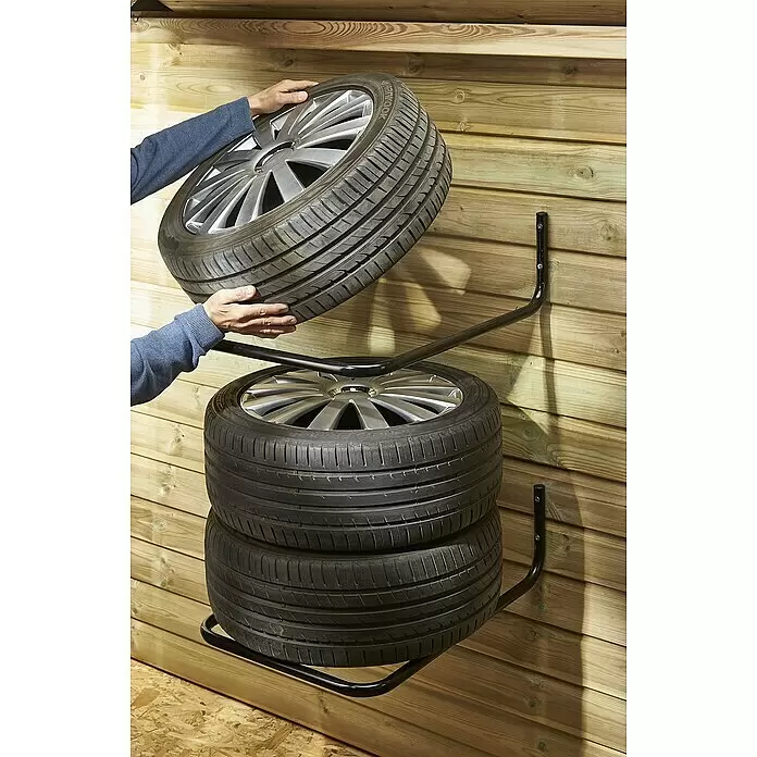 Mottez Reifen-Wandhalterung - Passend für: 4 Reifen, Traglast: 120 kg, 2 Stk. - Schwarzer Metall-Wandreifenhalter, der mehrere Autoreifen hält. Eine Person platziert einen Reifen auf dem Halter, was die Nutzung zeigt.