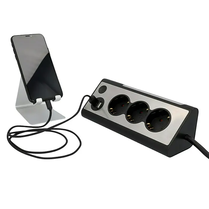 Tischsteckdose - 3-fach, Silber/Schwarz, 28 x 10,2 x 9 cm - Eine Steckdosenleiste mit drei Steckdosen und USB-Anschluss, an die ein Smartphone angeschlossen ist.