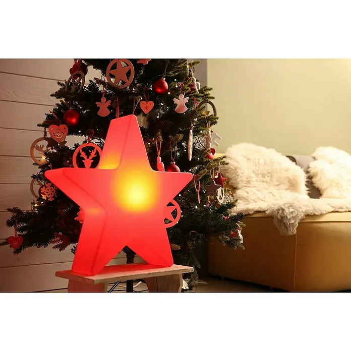 8 Seasons Design Shining Leuchtstern Star Mini - 9 W, Rot, L x B x H: 10 x 40 x 37 cm - Leuchtender roter Stern auf einem Hocker vor einem geschmückten Weihnachtsbaum, der festliche Stimmung verbreitet und die Weihnachtsdekoration hervorhebt.