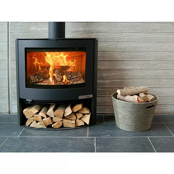 Aduro Kaminofen 15-2 - 6,5 kW, Raumheizvermögen: 334 m³, Material Verkleidung: Stahl, Schwarz - Schwarzer Holzofen mit hell brennendem Feuer, Brennholz im Sockel gestapelt und einem zusätzlichen Holzkorb daneben.