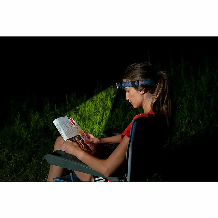 Coleman Linterna frontal CXS Headlam - 3 x 6,8 x 4 cm, 20 lm - 200 lm, IPX4 - Mujer leyendo en la oscuridad con un frontal. El frontal ilumina brillantemente, permitiendo la lectura al aire libre.