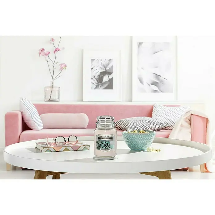 Yankee Candle Home Inspirations Duftkerze - Im Glas, Stony Cove, Large - Ein Yankee Candle Home Inspiration Duftkerze sitzt auf einem weißen Tisch, umgeben von dekorativen Elementen und einem rosa Sofa im Hintergrund.