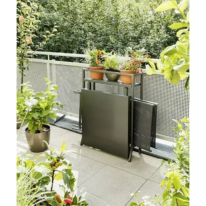 Sunfun Maja Balkonmöbel-Set - 3 -tlg., Anthrazit - Ein grauer Balkontisch mit Regal und verschiedenen Pflanzen in Töpfen steht auf einem gefliesten Balkon mit Grünpflanzen.