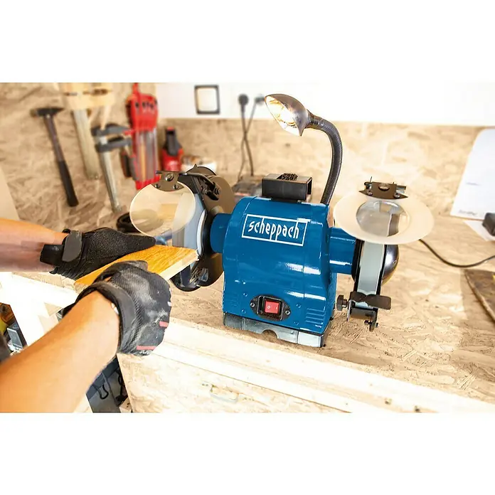 Scheppach Elektro-Doppelschleifer BG 200 - 550 W, Durchmesser Trockenschleifscheibe: 200 mm - Ein blauer Scheppach Doppelschleifer mit biegsamer Lampe wird zum Schleifen eines Holzstücks verwendet, was seine Funktionalität hervorhebt.