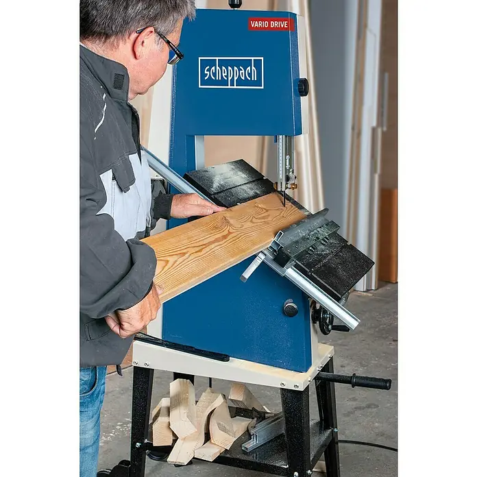 Scheppach Bandsäge BASA3 - 800 W, Durchlasshöhe: 205 mm, Durchlassbreite: 306 mm - Der Mann bedient eine Scheppach Bandsäge mit Vario Drive, um ein Holzbrett zu schneiden. Im Untergestell liegen Holzreste.