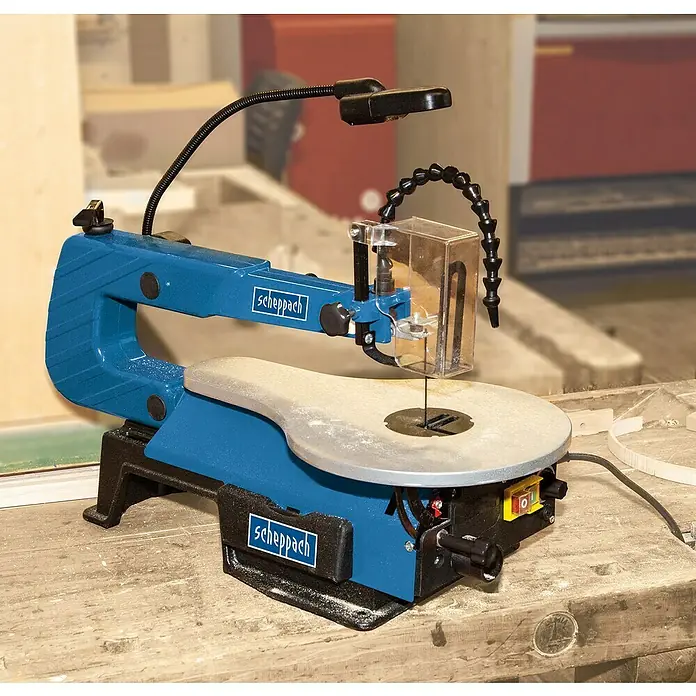 Scheppach Sierra de marquetería SD 1600 V - 120 W - Primer plano de una sierra de calar azul Scheppach con lámpara y protección transparente en un banco de trabajo.
