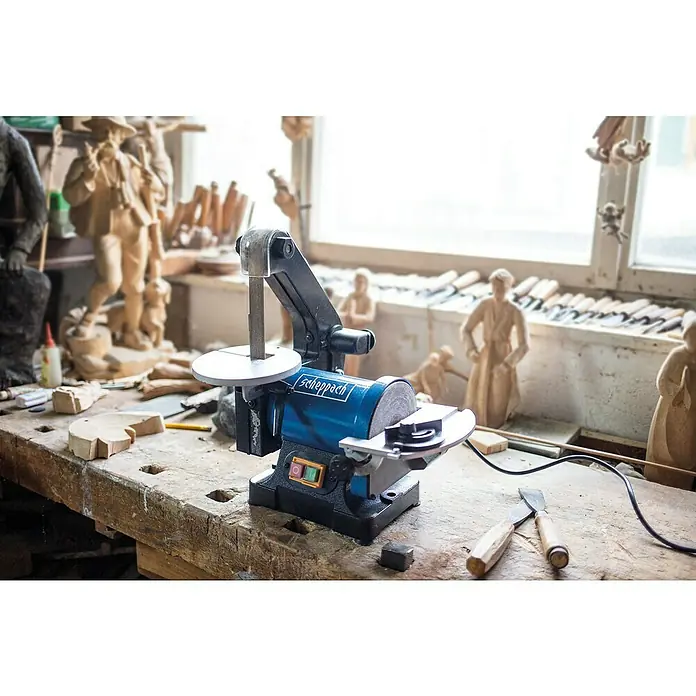 Scheppach Band- & Tellerschleifer BTS 700 - 250 W, Durchmesser Schleifteller: 125 mm - Nahaufnahme einer Scheppach Schleifmaschine auf einer Werkbank, umgeben von Holzbearbeitungswerkzeugen und Holzschnitzereien.