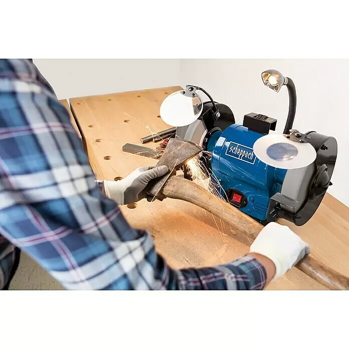 Scheppach Elektro-Doppelschleifer BG 150 - 370 W, Durchmesser Trockenschleifscheibe: 150 mm - Blaue Scheppach Doppelschleifmaschine schärft eine Axt, gehalten von behandschuhten Händen, Funken fliegen auf einer Werkbank.