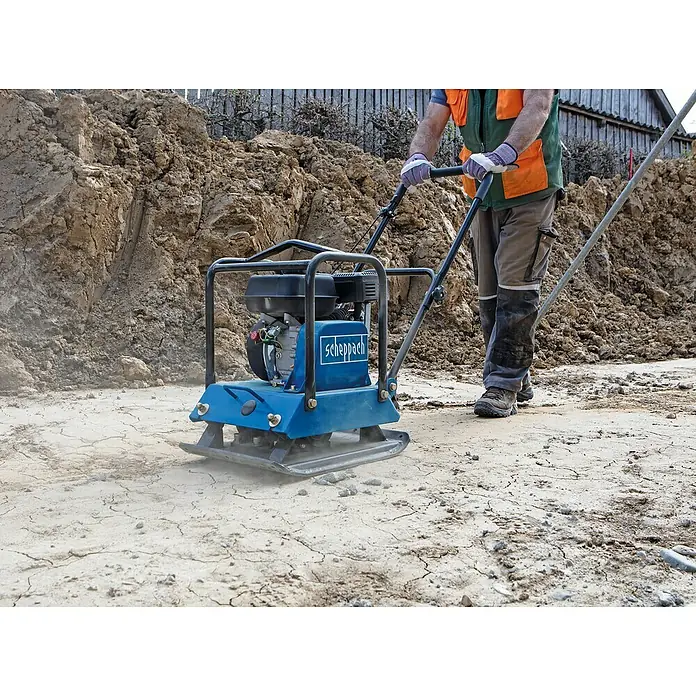 Scheppach Rüttelplatte HP 2200 S - 4,8 kW, Verdichtungsdruck: 25 kN - Ein Bauarbeiter verdichtet den Boden mit einer blauen Scheppach Vibrationsplatte. Ideal für den professionellen Einsatz im Garten- und Landschaftsbau.