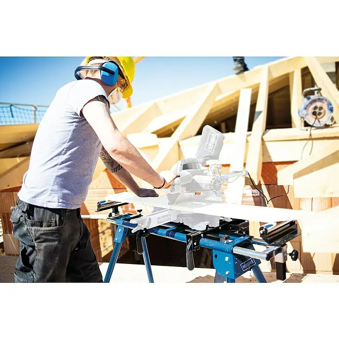 Scheppach Sägetisch UMF1600 - Geeignet für: Kappsägen, L x H: 1.000 x 810 mm - Ein Bauarbeiter mit gelbem Helm arbeitet an einer Scheppach-Säge mit blauem Gestell, um Holz für ein Bauprojekt zuzuschneiden.
