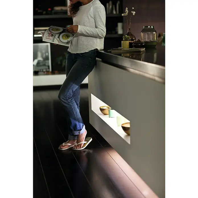 Philips Hue LED-Band Plus Basis - 2 m, RGBW - Frau liest Zeitschrift an Küchentheke mit dekorativer Beleuchtung.