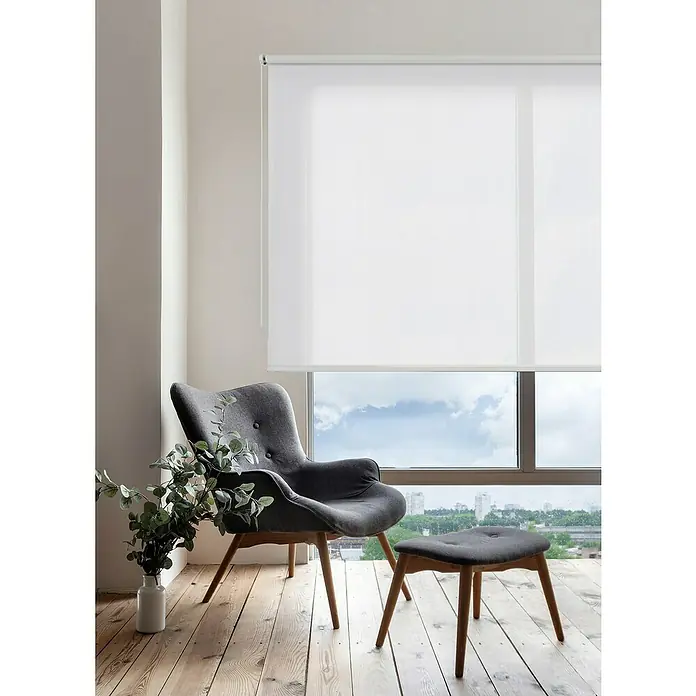 Estor enrollable Soft - An x Al: 200 x 250 cm, Blanco - Acogedor rincón de lectura con un sillón gris y una ventana con persianas enrollables blancas opacas para privacidad e iluminación suave.