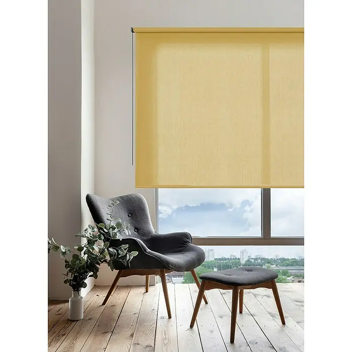 Estor enrollable Soft - An x Al: 140 x 250 cm, Mostaza - Las persianas enrollables amarillas frente a una ventana iluminan una habitación, con una silla y un reposapiés en primer plano.