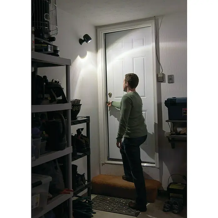 Mr. Beams LED-Strahler MB360XT - 200 lm, Braun - Eine Person öffnet eine weiße Tür in einer Garage, die von einer Wandlampe beleuchtet wird, neben einem Regal.