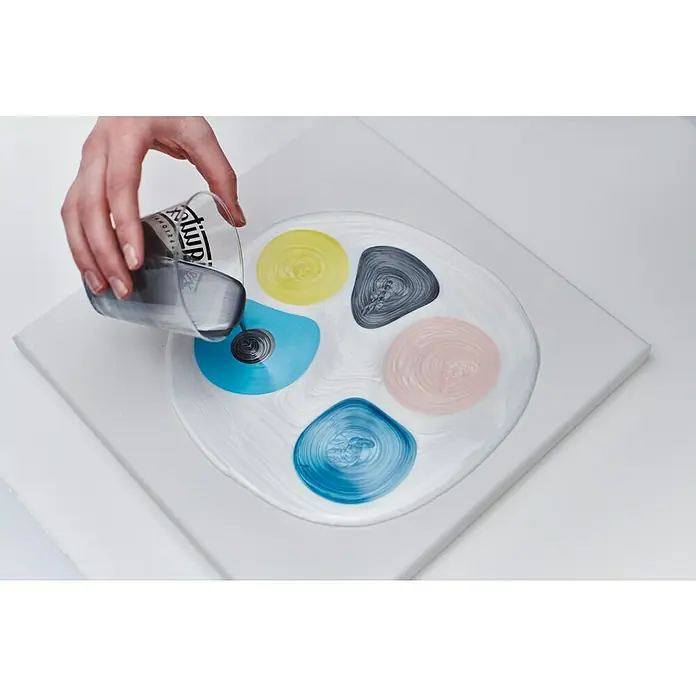 Liquitex Professional Gießmedium Irisierend - 473 ml, Transparent - Ein Glas wird über eine Leinwand mit Farbtupfern gegossen, wodurch ein faszinierendes Kunstwerk entsteht.