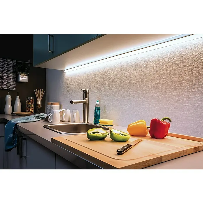 Paulmann MaxLED 500 LED-Band Function Tageslichtweiß Basisset - L x H: 10 m x 3 mm, Silber, Neutralweiß - Eine Küchenspüle mit Schneidebrett, auf dem geschnittene Paprika liegen, wird von einer hellen Unterbauleuchte beleuchtet.