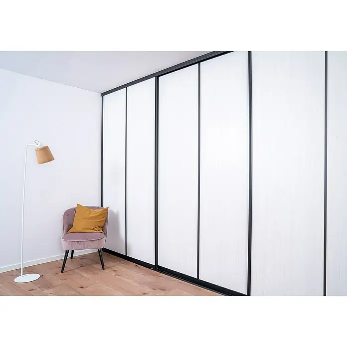 Room Plaza Easy Schiebetür-Bau-Set - Eiche Country/Pinie White, Farbe Beschlag: Schwarz - Ein modernes Schlafzimmer mit einem großen Schrank mit weißen Schiebetüren und einem schlanken schwarzen Rahmen. Ein bequemer Sessel steht daneben.