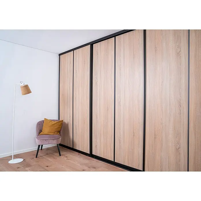 Room Plaza Easy Schiebetür-Bau-Set - Eiche geplankt/Eiche Trüffel, Farbe Beschlag: Schwarz - Das Bild zeigt einen modernen Schrank mit Schiebetüren in einem hellen Raum mit einer Lampe und einem Stuhl. Der Schrank dominiert die Szene.