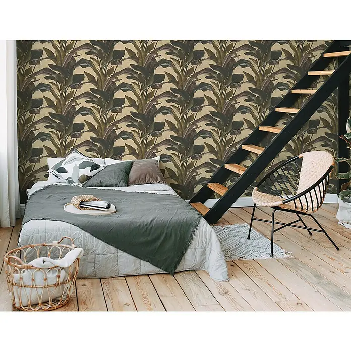 A.S. Création Metropolitan Stories II Vliestapete Blätter - Gold, Floral, 10,05 x 0,53 m - Schlafzimmer mit Doppelbett, Leiterregal, Korbstuhl und Zimmerpflanze vor einer Wand mit floralem Muster.