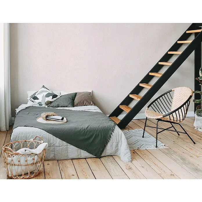 A.S. Création Metropolitan Stories II Vliestapete - Creme/Beige, Uni, 10,05 x 0,53 m, Matt - Schlafzimmer mit gemütlichem Bett, Leiter zum Hochbett und einem einladenden Rattansessel auf einem hellen Holzboden.