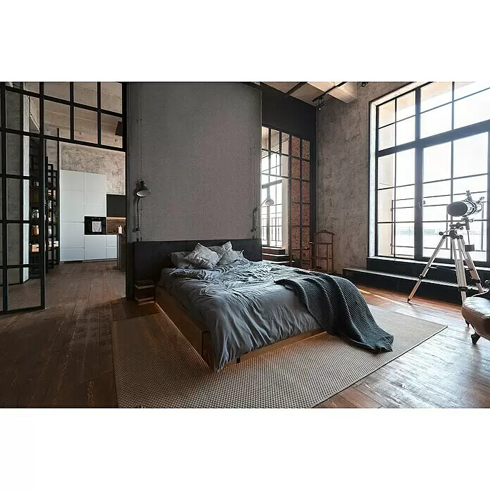 A.S. Création Metropolitan Stories II Vliestapete - Dunkelgrau, Uni, 10,05 x 0,53 m, Matt - Modernes Industriezimmer mit grauem Bett, grauer Bettwäsche und diskreter Unterbeleuchtung auf hellem Teppich und dunklem Holzboden.