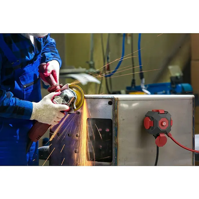 Steckdosenball - Grau/Rot, 1,4 m, IP44 - Ein Arbeiter schleift Metall mit einer Flex, wobei Funken sprühen, und ein Mehrfachstecker ist sichtbar.