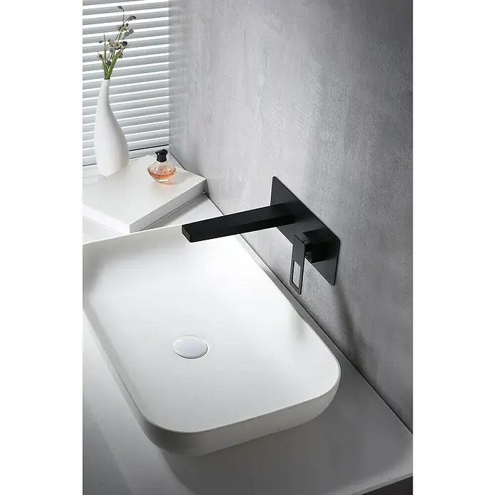 Imex Suecia Grifo de lavabo - Negro - Un lavabo moderno con un elegante grifo negro contra una pared gris, complementado con un jarrón y perfume.