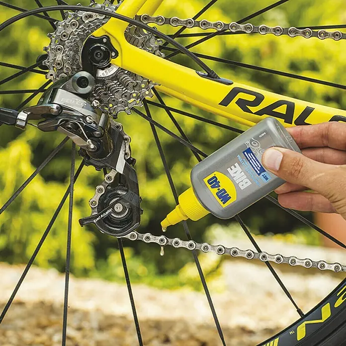 WD-40 Bike Lubricante ambientes húmedos - 100 ml, Apto para: Cadenas de bicicleta - Primer plano de una persona aplicando lubricante de cadena WD-40 BIKE a una cadena de bicicleta para su mantenimiento.