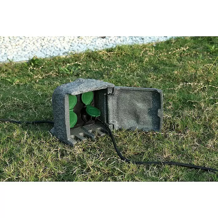 Voltomat Baustromverteiler Power Rock - Anzahl Steckdosen Schuko: 4 Stk., IP44 - Graue, felsähnliche Outdoor-Steckdosenbox mit grünen Abdeckungen, im Gras mit schwarzem Kabel.