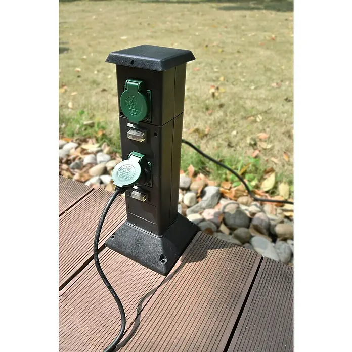 Voltolux Energiesäule - Anzahl Steckdosen Schuko: 4 Stk., IP44 - Eine Außensteckdose mit zwei grünen Steckdosen auf einer Holzterrasse, bereit für den Anschluss von Geräten im Freien.