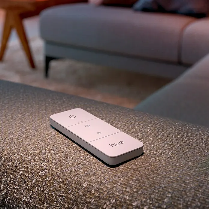 Philips Hue Dimmcontroller V2 - L x B x H: 1,5 x 8 x 12,5 cm - Nahaufnahme einer Philips Hue Fernbedienung auf einem Sofa, die Lichtsteuerung für ein smartes Zuhause ermöglicht.