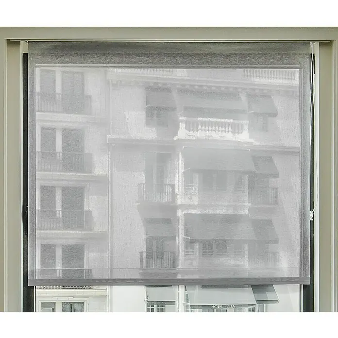 Estor enrollable Bahamas - An x Al: 90 x 250 cm, Gris - Una persiana enrollable gris cubre una ventana, revelando un edificio detrás. La persiana ofrece privacidad y deja entrar la luz.