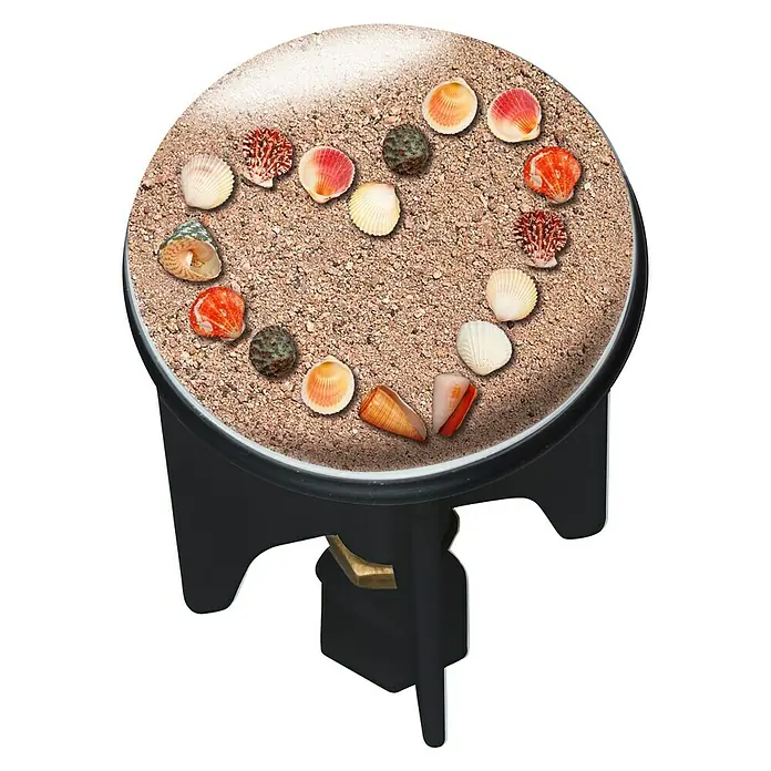 Wenko Design-Excenterstopfen Pluggy Heartbeach - Heartbeach, Durchmesser: 3,9 cm - Nahaufnahme einer Miniatur-Strandszene auf einem kleinen schwarzen Ständer. Die Szene enthält Sand und verschiedene Muscheln.