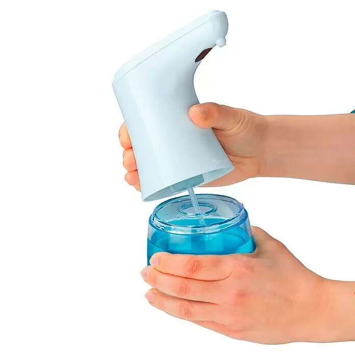 Wenko Desinfektionsmittelspender Diala - Weiß, L x B x H: 19 x 12 x 23 cm - Hände montieren einen weißen automatischen Seifenspender mit transparentem Sockel, gefüllt mit blauer Flüssigkeit.