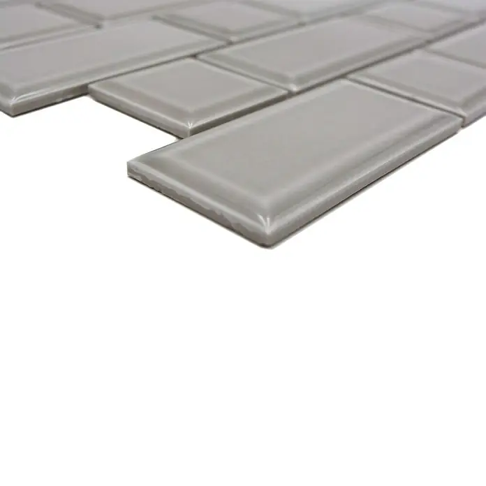 Mosaikfliese Metro Uni CG M04CM - 29,4 x 29,1 cm, Grau, Glänzend - Nahaufnahme von grauen rechteckigen Wandfliesen mit glänzender Oberfläche, die im Fischgrätenmuster verlegt sind.
